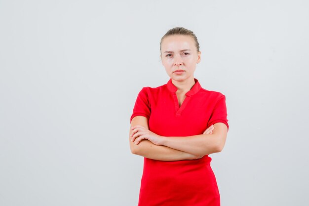 赤いTシャツで腕を組んで立っていると厳格に見える若い女性