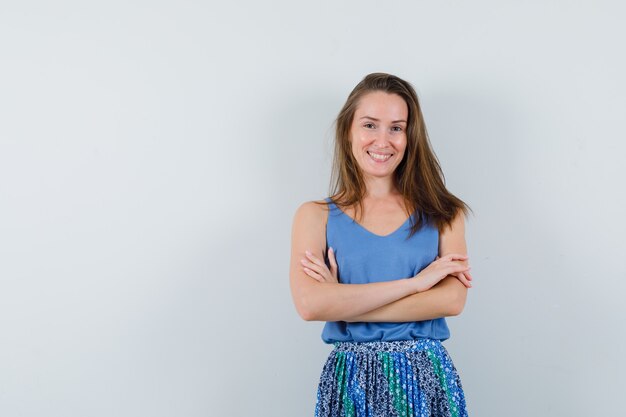 Young lady standing with crossed arms in singlet, skirt and looking cheery. front view.