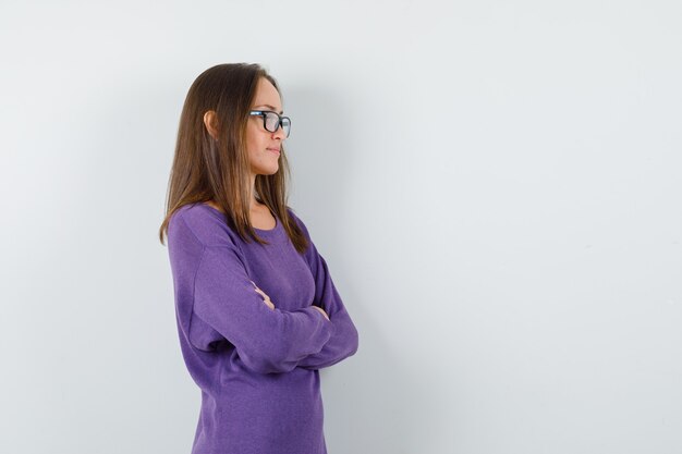 Young lady standing with crossed arms in violet shirt and looking pensive. .