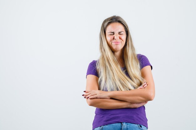 Young lady standing with crossed arms in violet t-shirt, jeans and looking happy. front view.