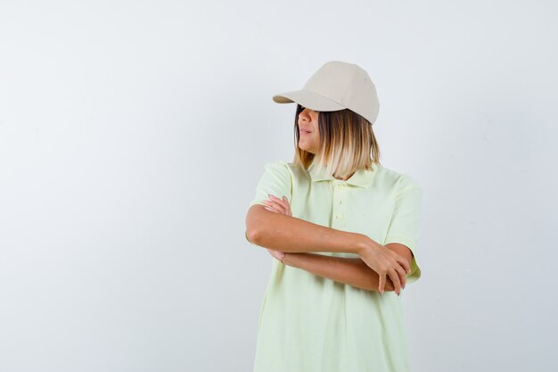 티셔츠, 모자에서 멀리보고 자신감, 전면보기를 보면서 팔을 교차 서있는 젊은 아가씨.