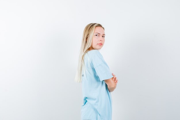 Young lady standing with crossed arms while looking over shoulder in t-shirt and looking confident , front view.