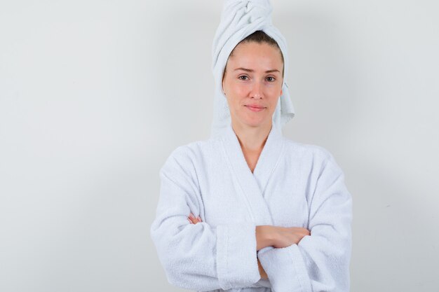 Young lady standing with crossed arms in white bathrobe, towel and looking confident. front view.