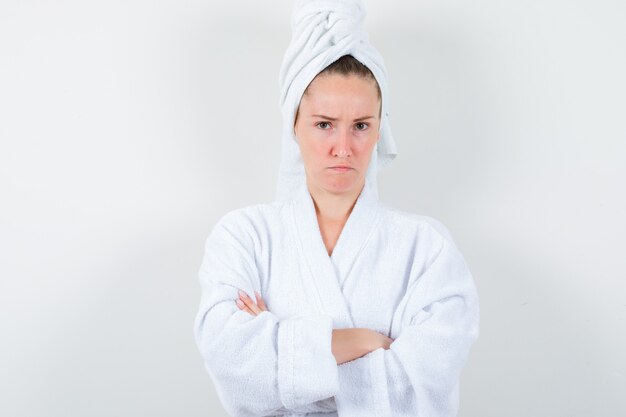 白いバスローブ、タオルで腕を組んで立っていると憤慨している若い女性。正面図。