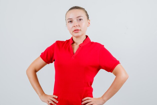 Young lady standing with hands on waist in red t-shirt and looking confident