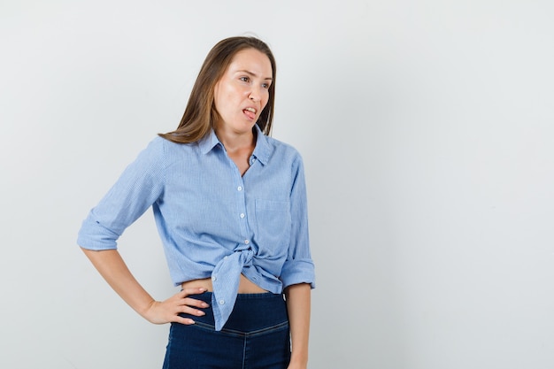 Young lady sticking out tongue in blue shirt, pants and looking disgusted.