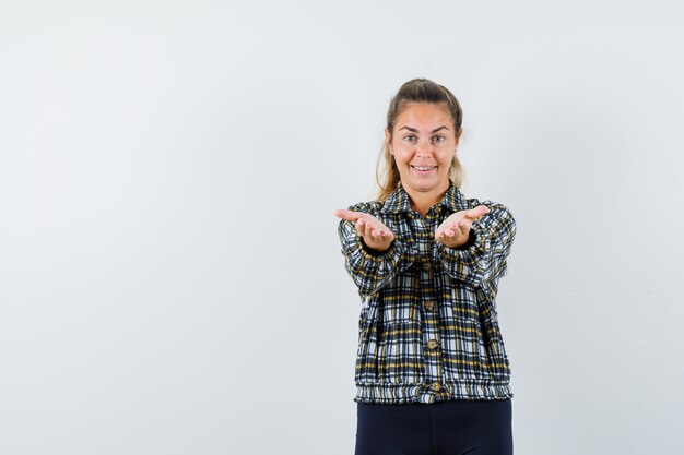 Young lady stretching arms in shirt, shorts and looking cheerful. front view.