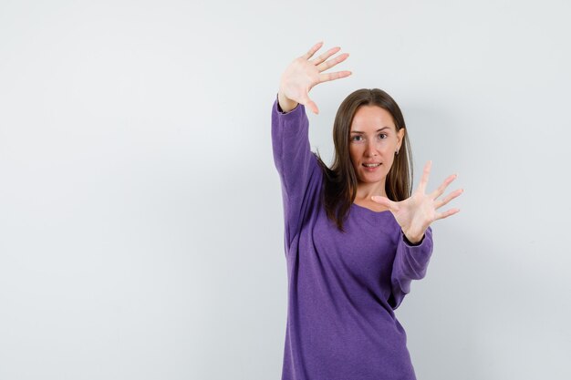 Young lady stretching arms and showing palms in violet shirt front view.