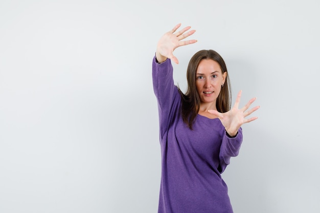 若い女性は腕を伸ばし、紫のシャツの正面図で手のひらを示しています。