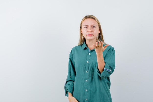 Young lady stretching hand in puzzled gesture in green shirt and looking serious.