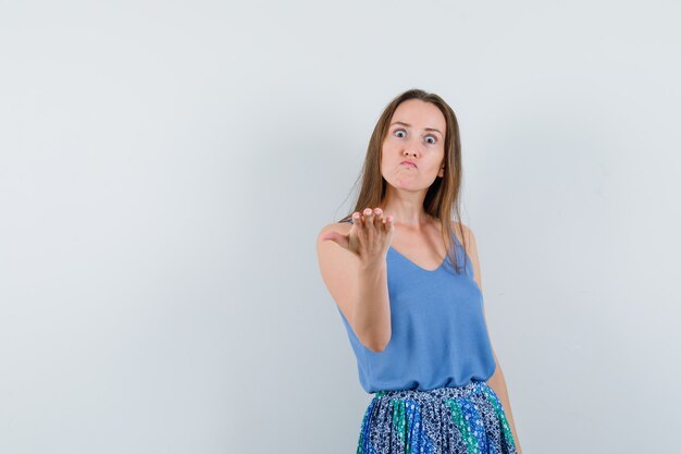 Young lady stretching hand in puzzled gesture in singlet, skirt front view.