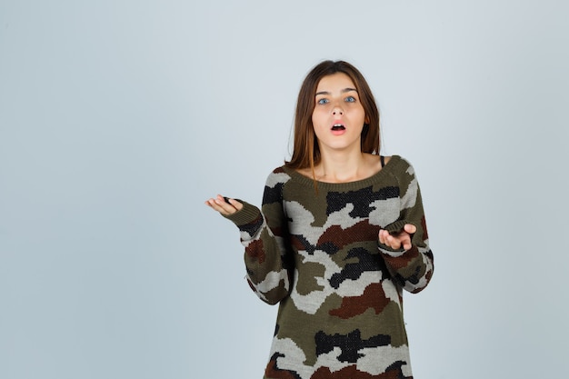 Young lady stretching hand in questioning gesture in sweater and looking perplexed