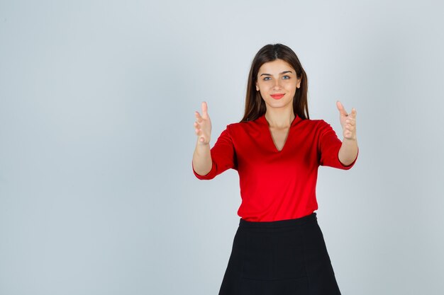 Young lady stretching hands as showing width in red blouse, black skirt and looking happy