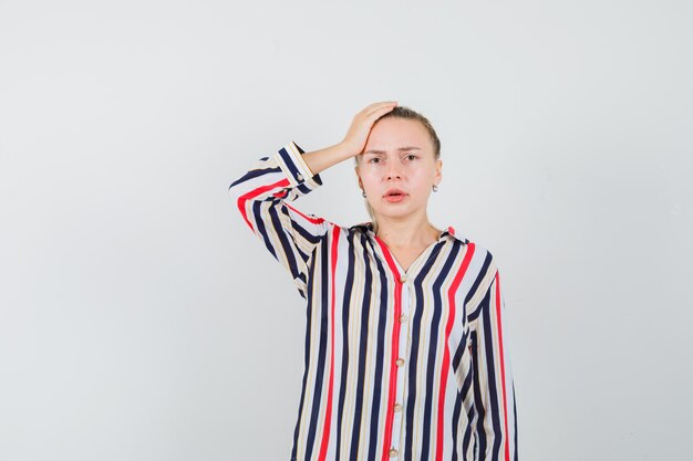 Young lady in striped shirt holding hand on head and looking downcast