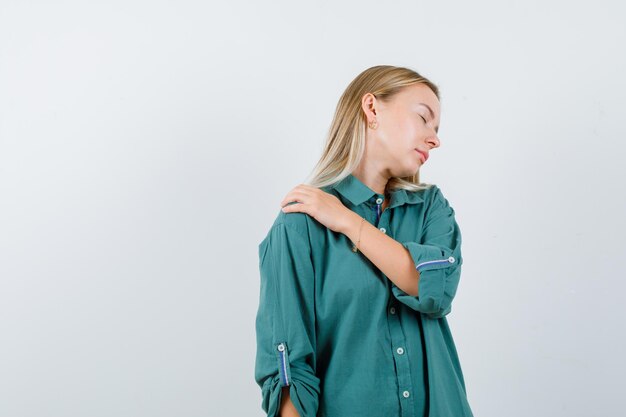 Young lady suffering from shoulder pain in green shirt and looking tired.