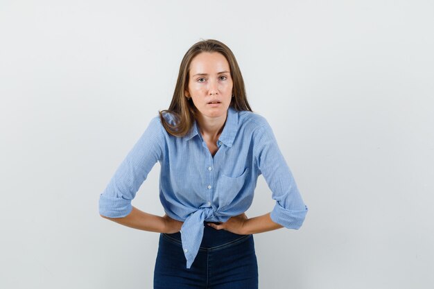 Young lady suffering from stomach pain in blue shirt, pants and looking languish.