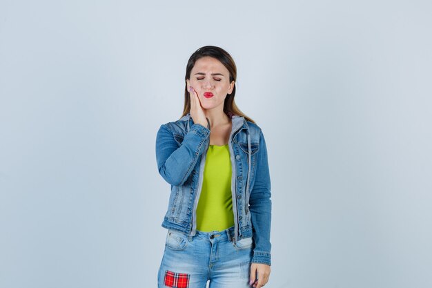 Young lady suffering from terrible toothache in denim outfit and looking bothered. front view.