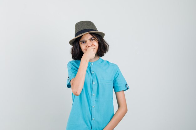 Young lady suffering from toothache in blue shirt, hat and looking troubled.