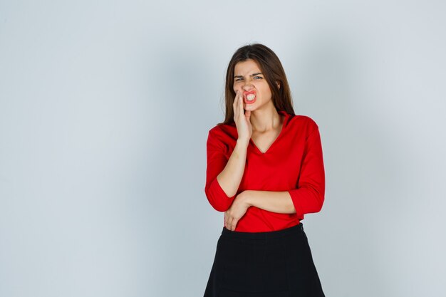 Young lady suffering from toothache in red blouse, skirt and looking unwell