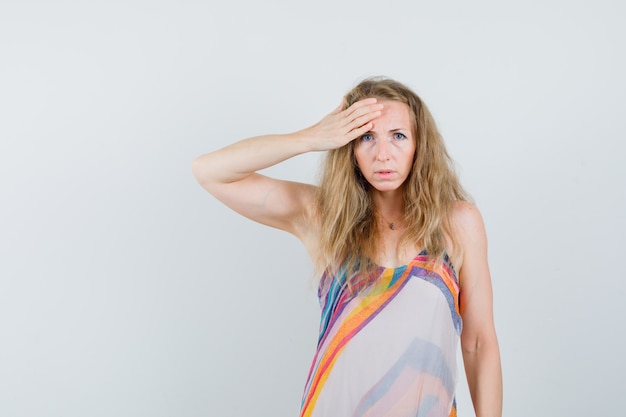 Young lady in summer dress holding hand on forehead and looking puzzled 