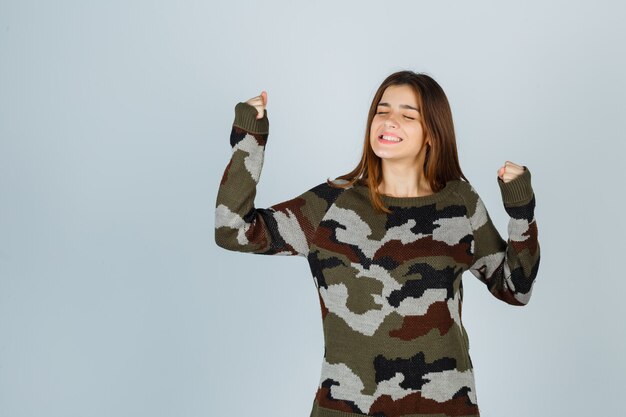 Young lady in sweater showing winner gesture and looking lucky