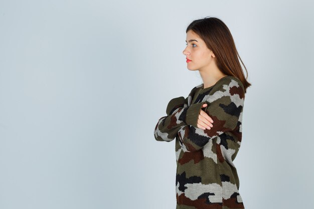 Young lady in sweater, skirt hugging herself and looking pensive