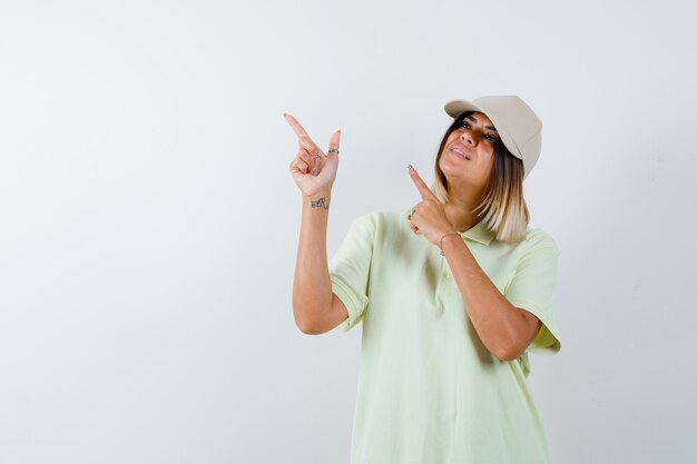 Девушка в футболке, кепка, указывающая на верхний левый угол и радостная, вид спереди.