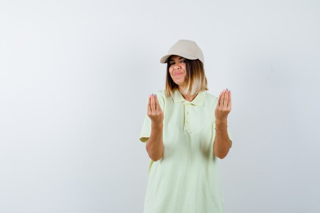 Young lady in t-shirt, cap showing Italian gesture and looking delighted , front view.