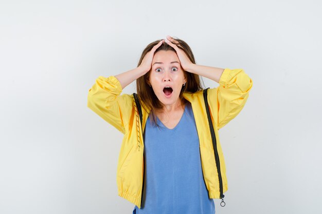 Young lady in t-shirt clasping head in hands and looking excited , front view.