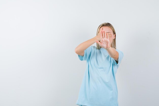 Young lady in t-shirt covering eyes with hand while showing stop gesture isolated