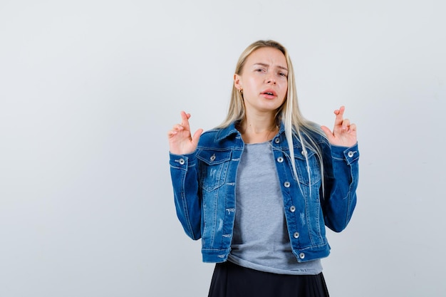 Tシャツ、デニムジャケット、交差した指を見せてきれいに見えるスカートの若い女性