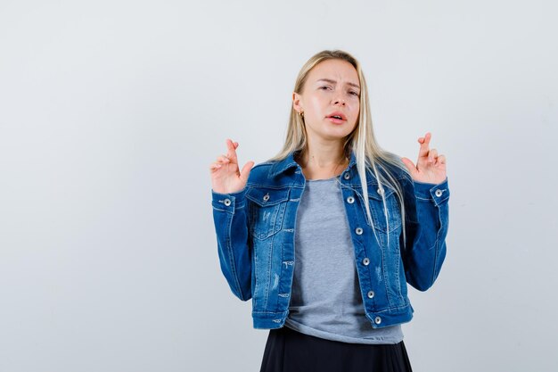 Young lady in t-shirt, denim jacket, skirt showing crossed fingers and looking pretty