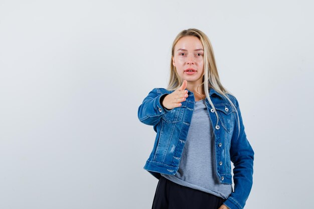 Young lady in t-shirt, denim jacket, skirt showing something and looking confident