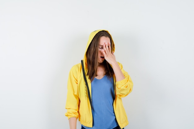 Young lady in t-shirt holding hand on face and looking forgetful, front view.