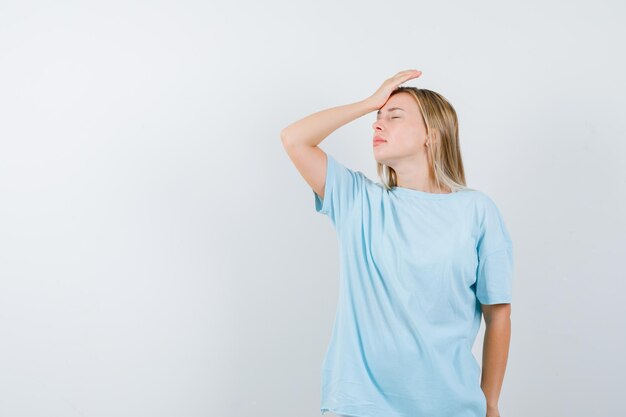 Young lady in t-shirt holding hand on forehead and looking exhausted isolated