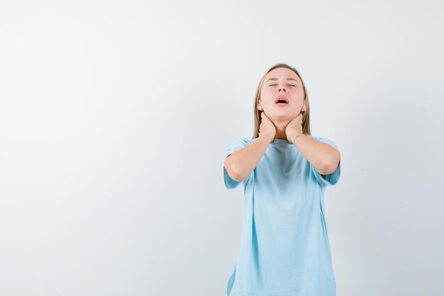 Young lady in t-shirt holding hands on neck and looking fatigued isolated