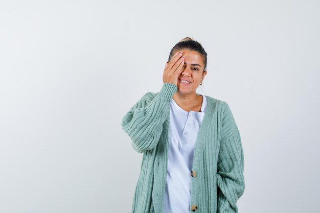 Young lady in t-shirt, jacket covering eye with hand and looking joyful