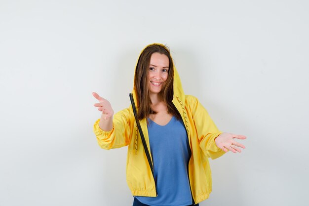 Young lady in t-shirt, jacket doing welcome gesture and looking cheerful