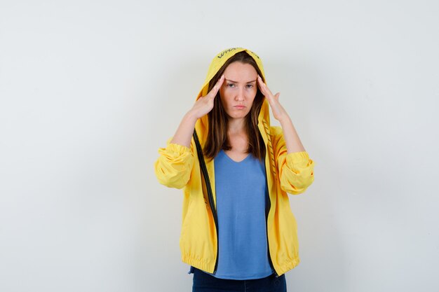 Young lady in t-shirt, jacket holding fingers on temples and looking fatigued , front view.