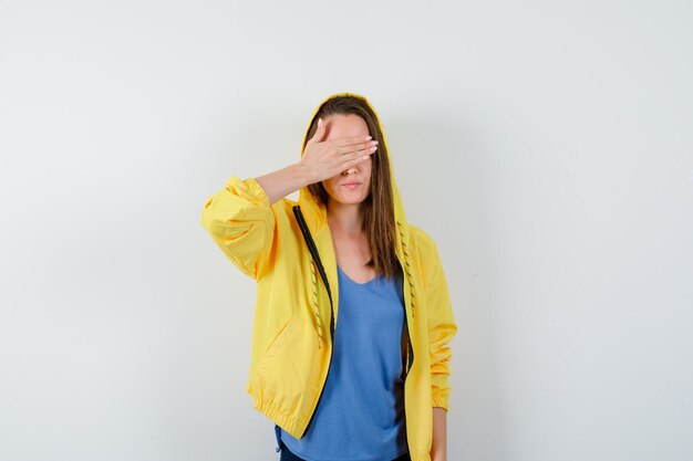 Young lady in t-shirt, jacket holding hand on eyes and looking calm