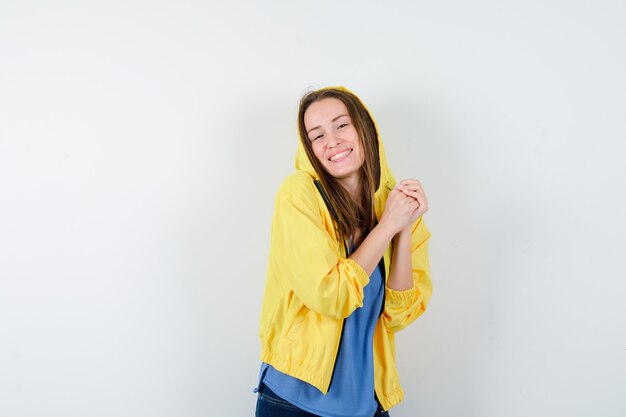 Young lady in t-shirt, jacket holding hands clasped and looking happy, front view.