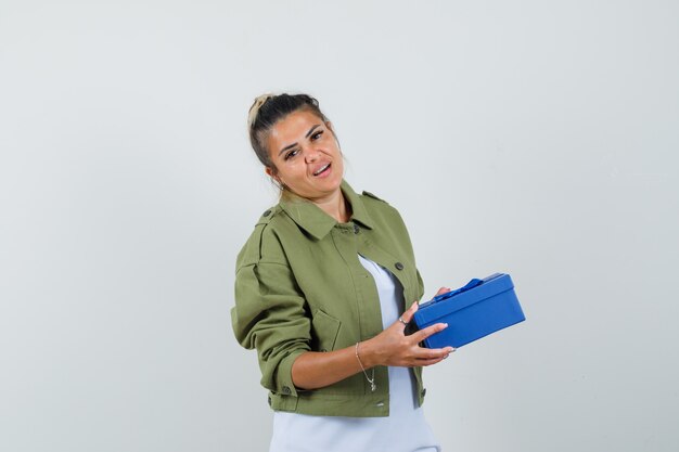 Молодая дама в куртке футболки держит подарочную коробку и выглядит уверенно