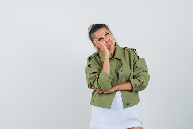 Young lady in t-shirt jacket leaning cheek on palm and looking fatigued