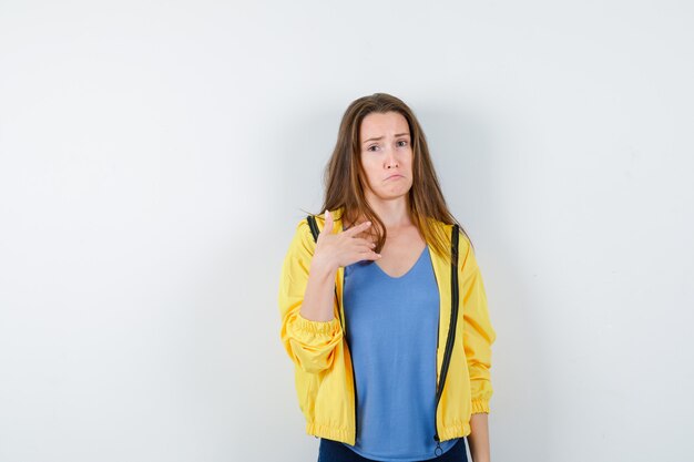Young lady in t-shirt, jacket pointing at herself, curving lips and looking innocent , front view.