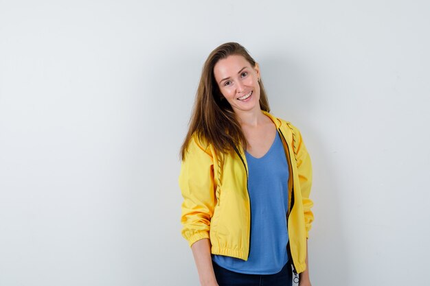 Young lady in t-shirt, jacket posing while standing and looking cheerful, front view.