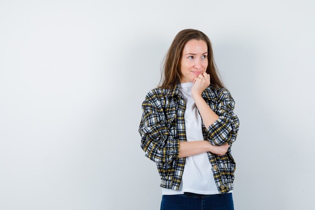 Young lady in t-shirt, jacket propping chin on hand and looking dreamy , front view.