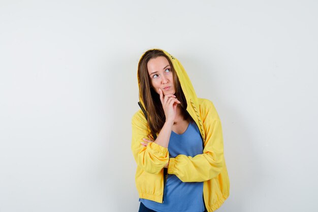 Young lady in t-shirt, jacket propping chin on hand and looking dreamy