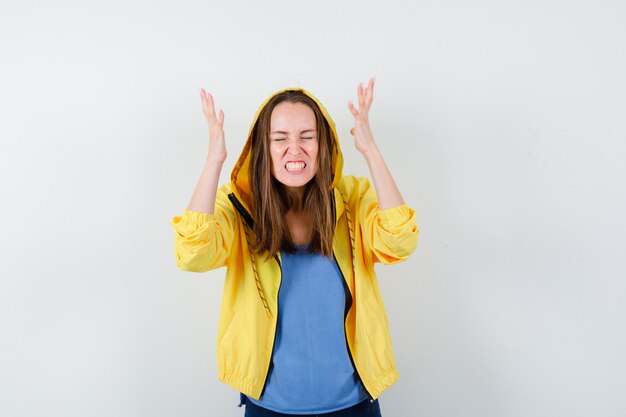 Free photo young lady in t-shirt, jacket raising hands, clenching teeth and looking agitated , front view.