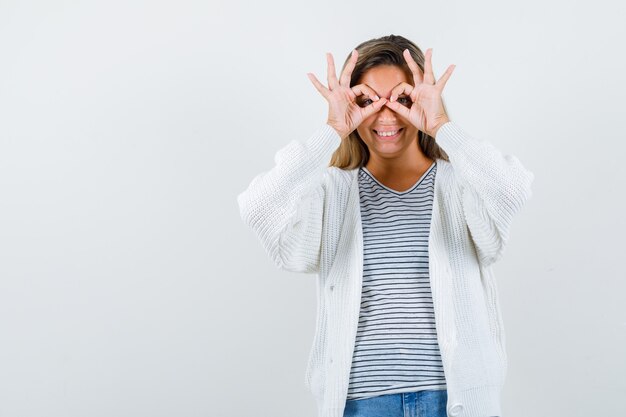 Young lady in t-shirt, jacket showing glasses gesture and looking cheerful , front view.