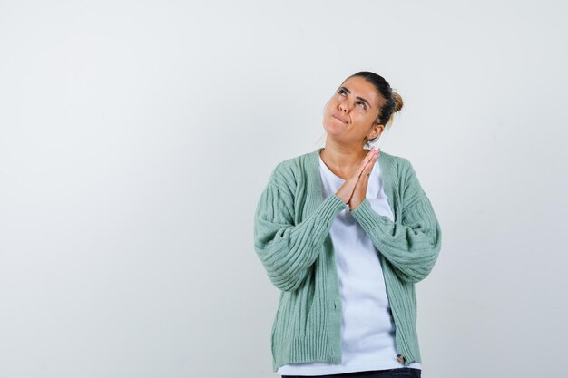 Young lady in t-shirt, jacket showing praying gesture and looking hopeful